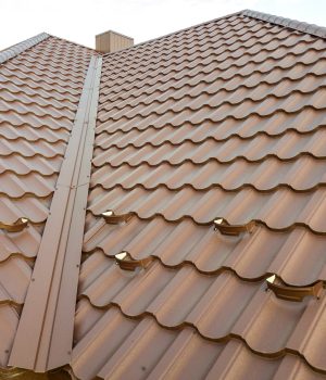 Detail of a house roof surface covered with brown metal tile sheets.