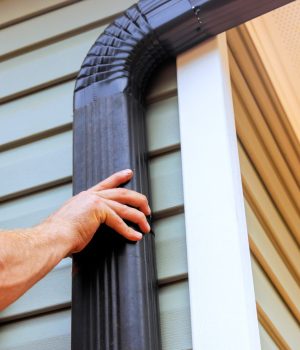 On roof, worker is installing rain gutter fitting downpipe downspout bend