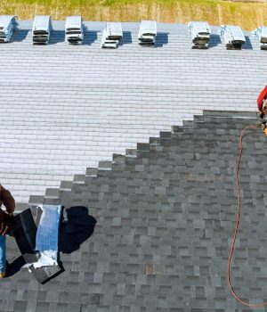 Aerial view in worker hands installing bitumen roof shingles with air hammer and nail